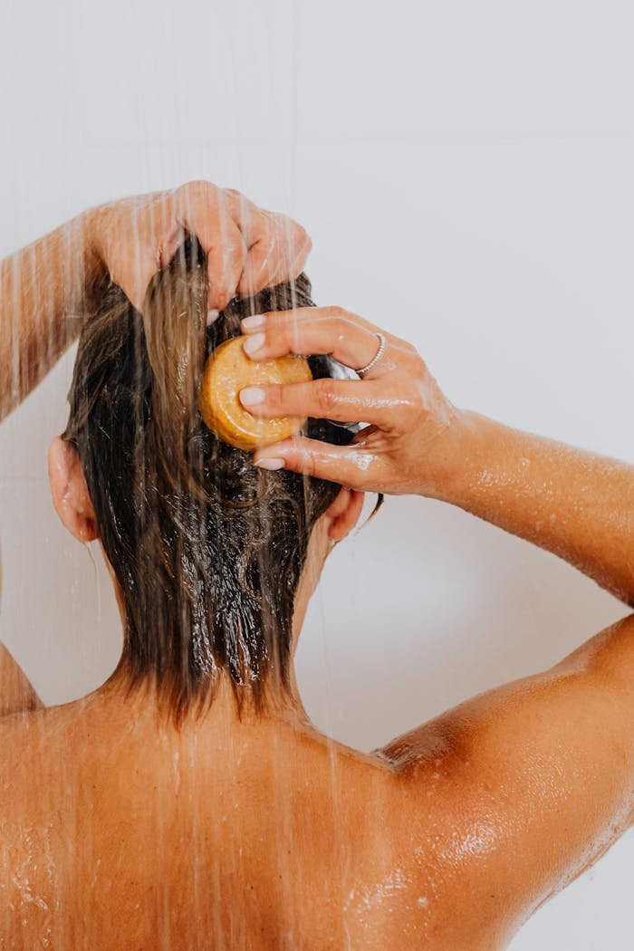 Back view of a woman washing her hair in the shower under running water.