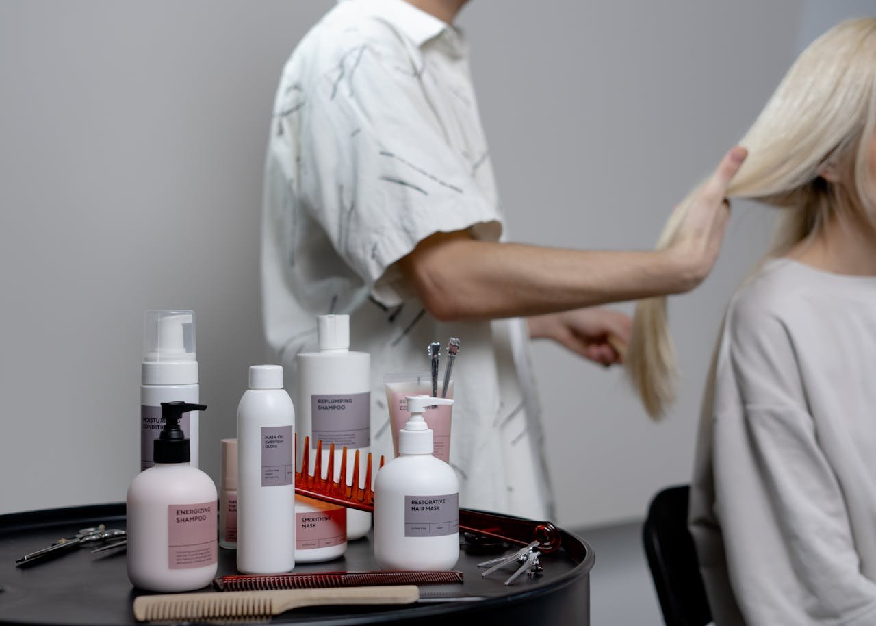 A hairdresser styling a blonde woman's hair in a salon, showcasing hair care products on a table.